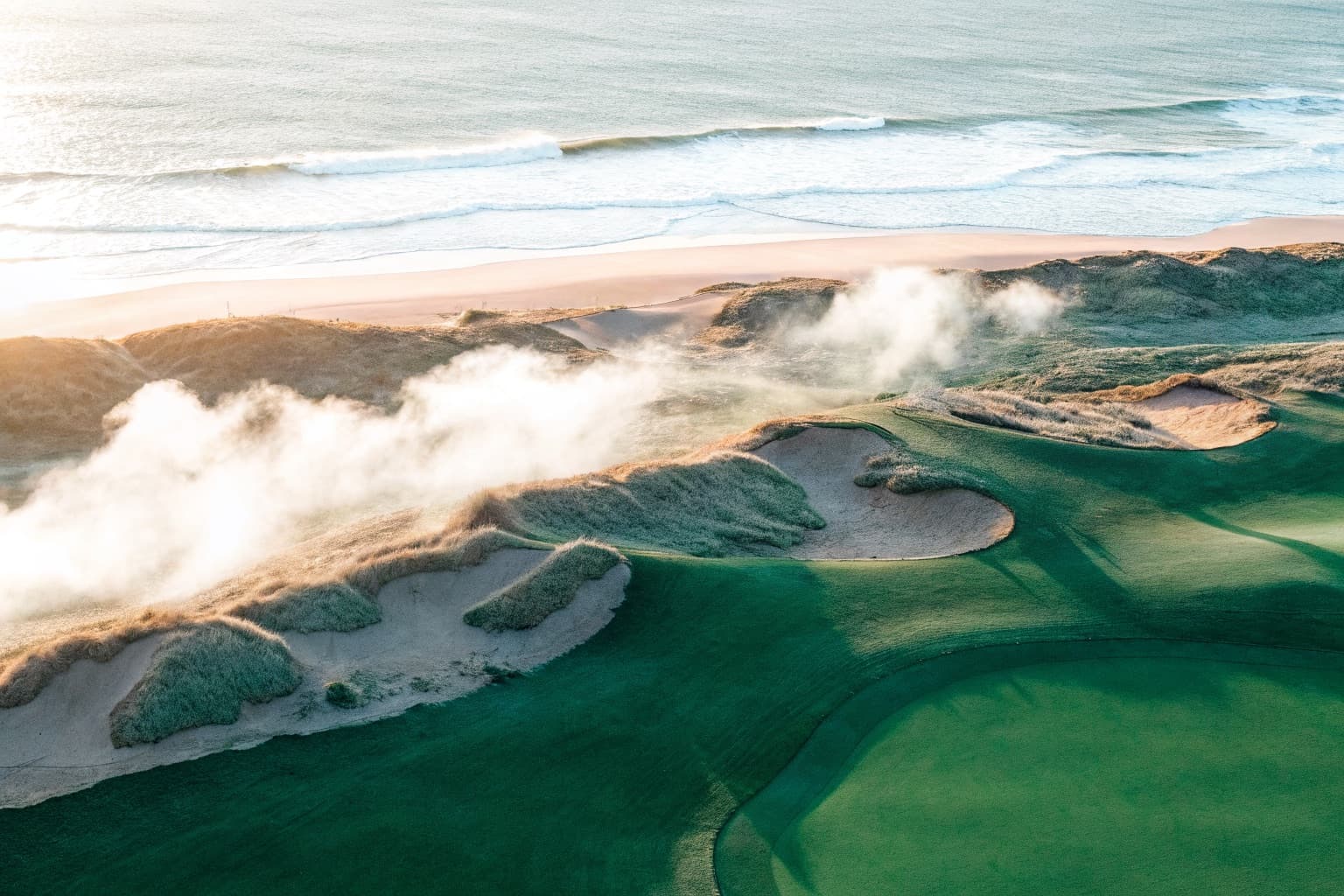 Aerial view of a dramatic links golf course on coastal cliffs with morning mist and ocean