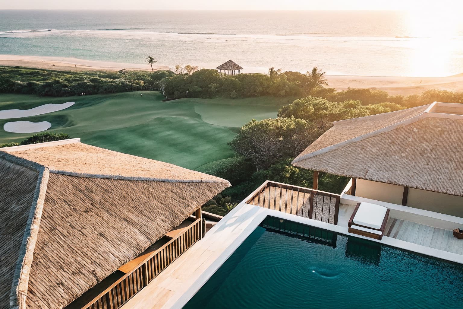 Aerial view of a luxury Bali resort with infinity pool overlooking a golf course and ocean at sunset